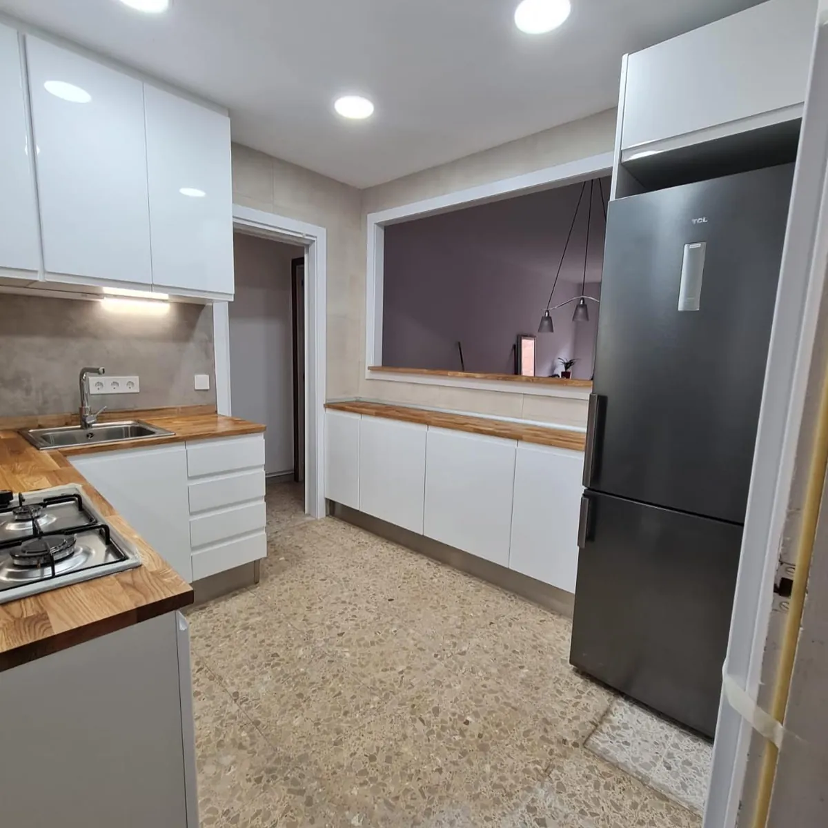Cocina blanca abierta al salón con encimera de madera y electrodomésticos integrados